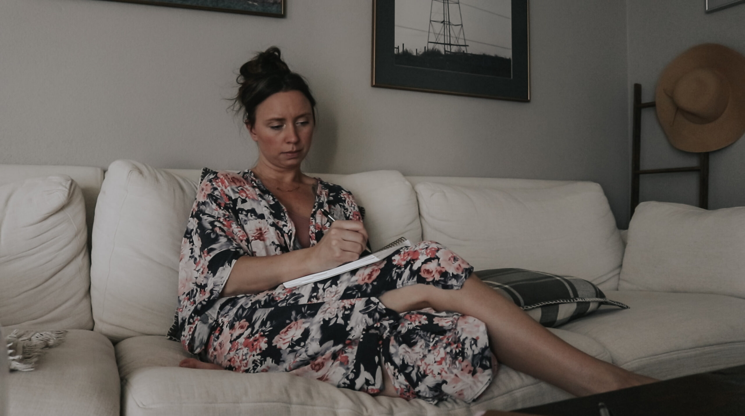 Christian homemaker sits on couch in a flowery robe writing in her journal.